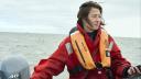 Portrait of a woman (Hailley) on a speedboat. She is holding the steering wheel on the left and looking to the right. She is wearing an orange life jacket.