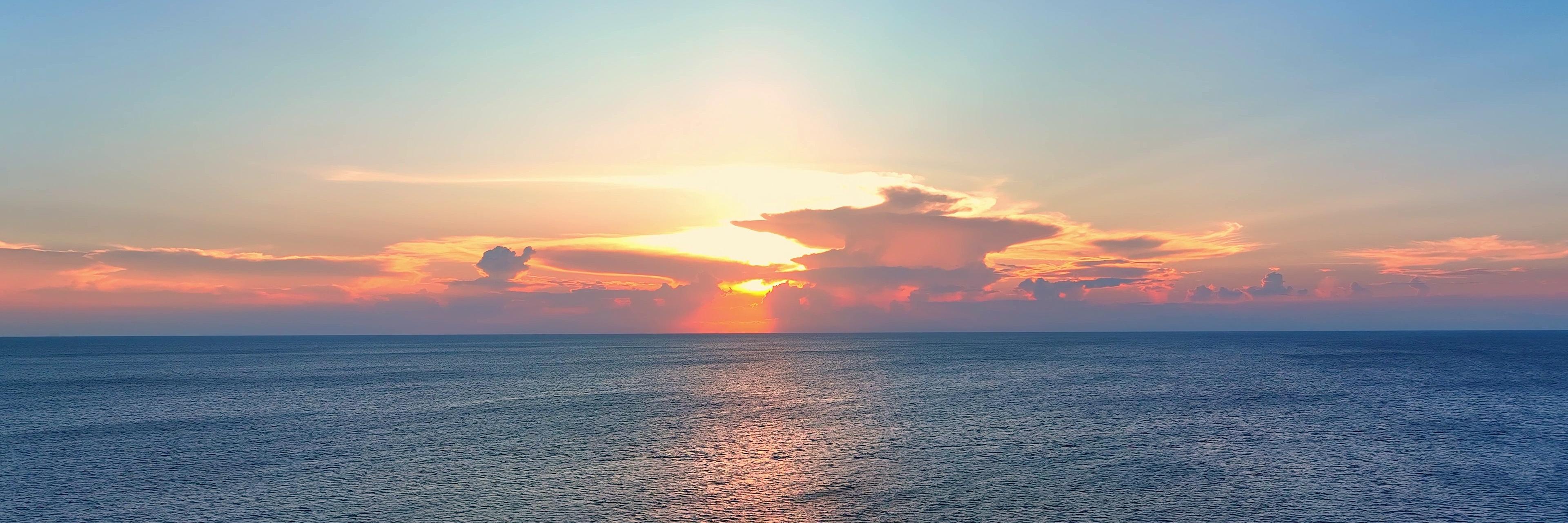 De oceaan bij zonsondergang met de zon die door de wolken schijnt.